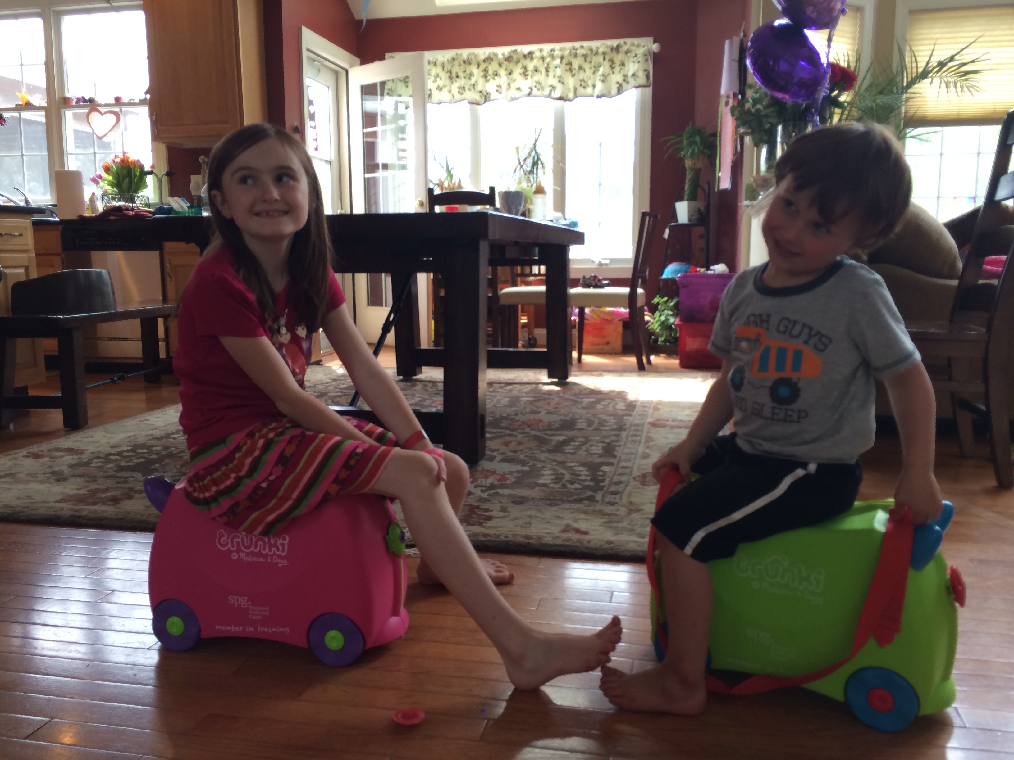 a boy and girl sitting on toy suitcases in a room