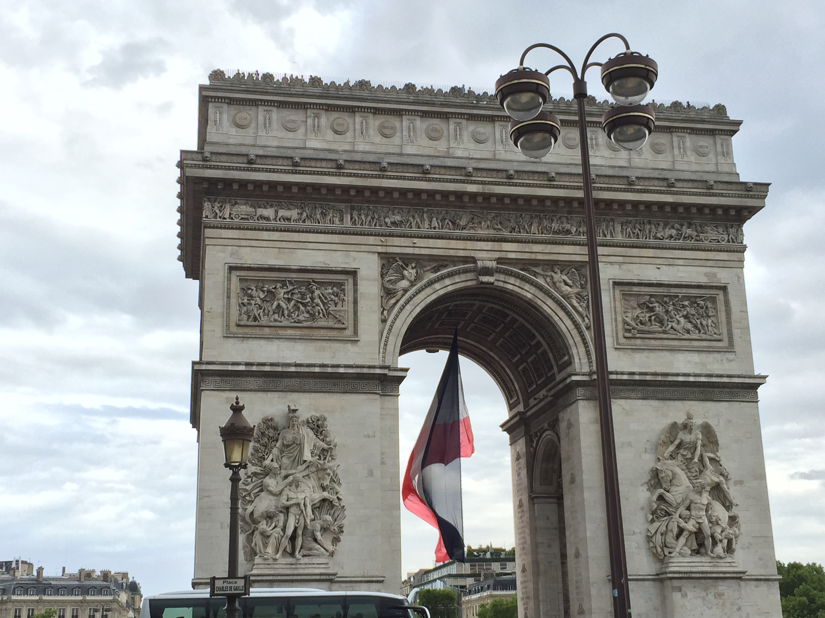 a large stone arch with a flag from the top with Arc de Triomphe in the background