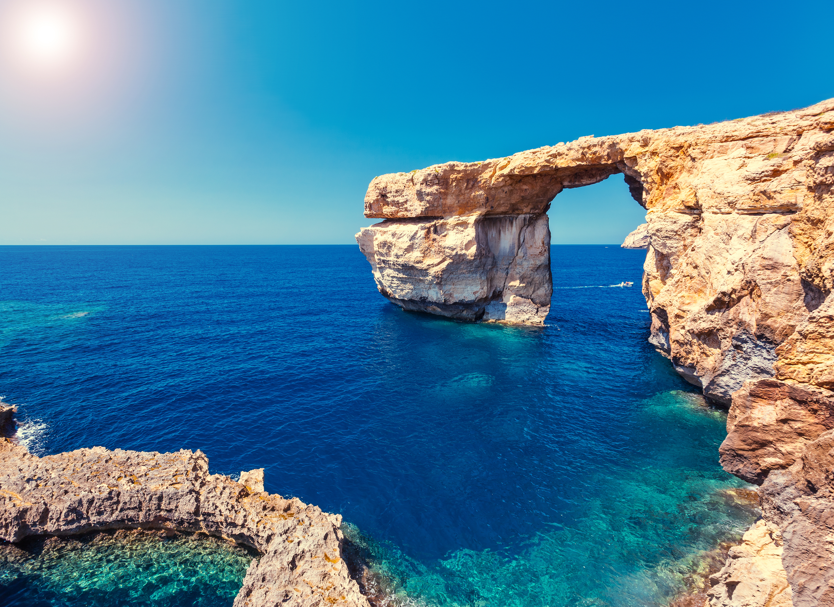 a rock arch over water with Gozo in the background