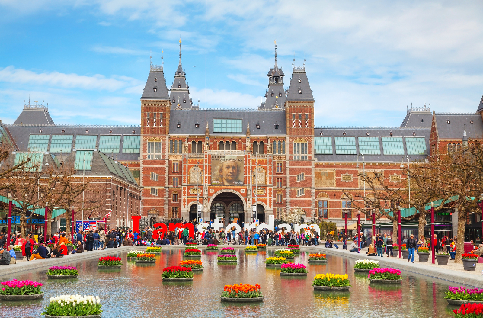 a large building with a pond with flowers in it with Rijksmuseum in the background