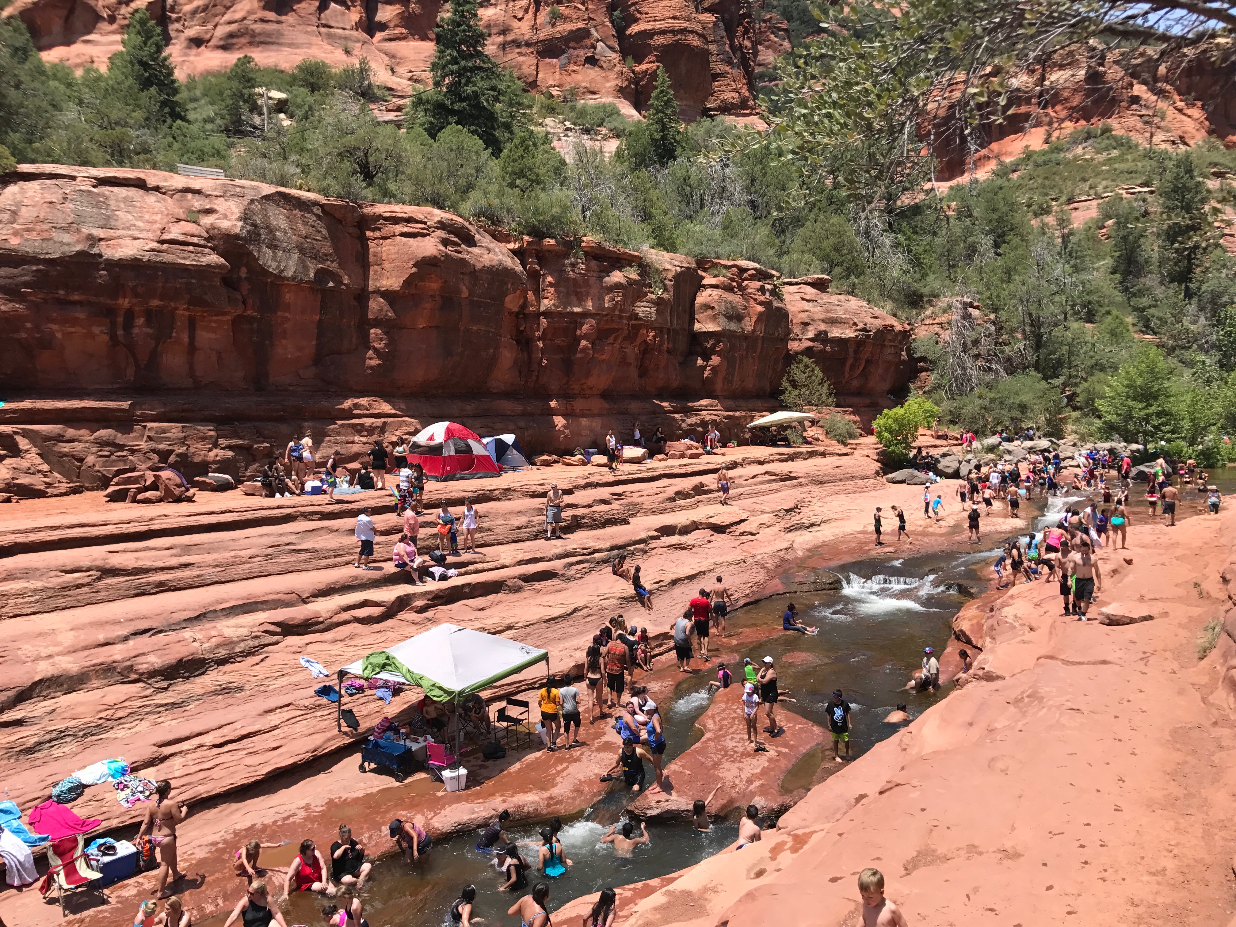 a group of people in a river with Slide Rock State Park in the background