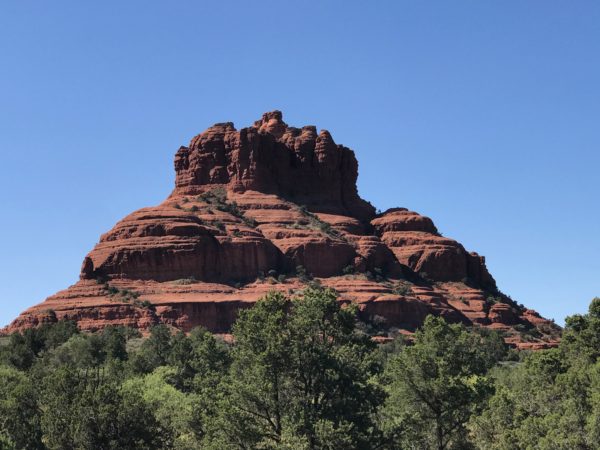a red rock mountain with trees in the background with Bell Rock in the background