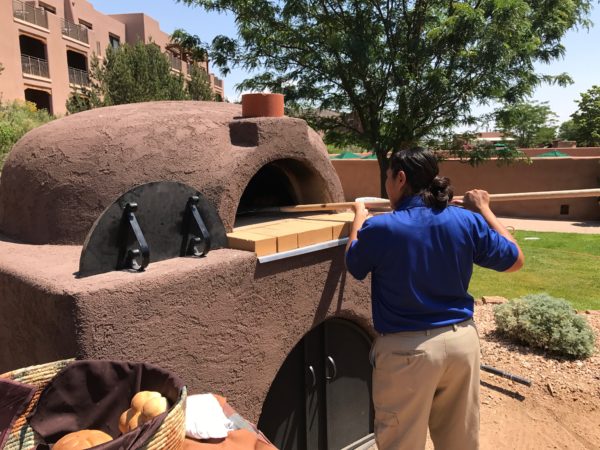 a woman putting pizza in a wood oven