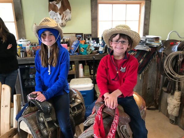 two children sitting on saddles in a room with a cowgirl's head