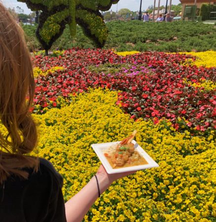a person holding a plate of food in front of a flower garden