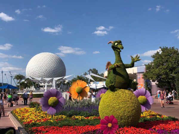 a topiary in a garden with flowers and a sphere in the background with Epcot in the background