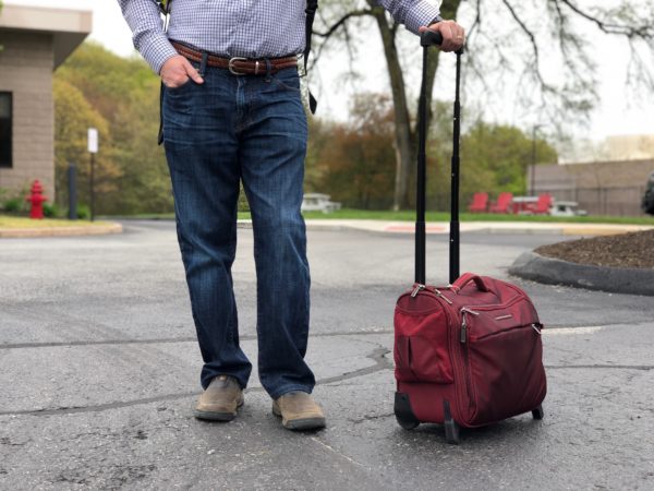 a man standing with his hands in his pockets next to a suitcase