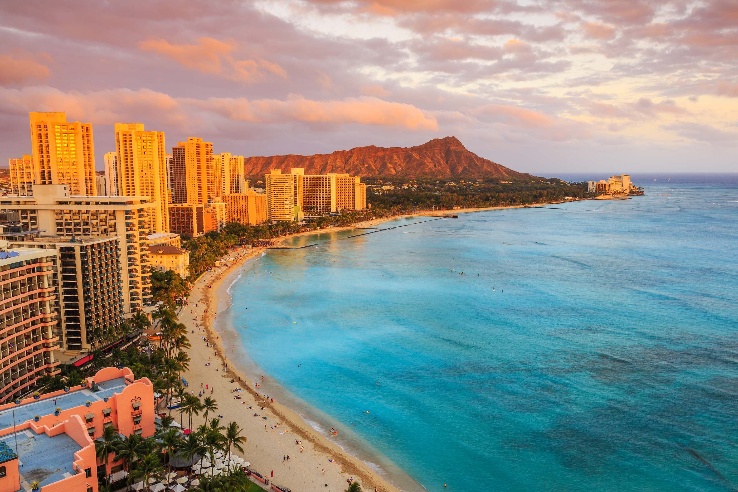 a beach with buildings and a body of water with Diamond Head in the background