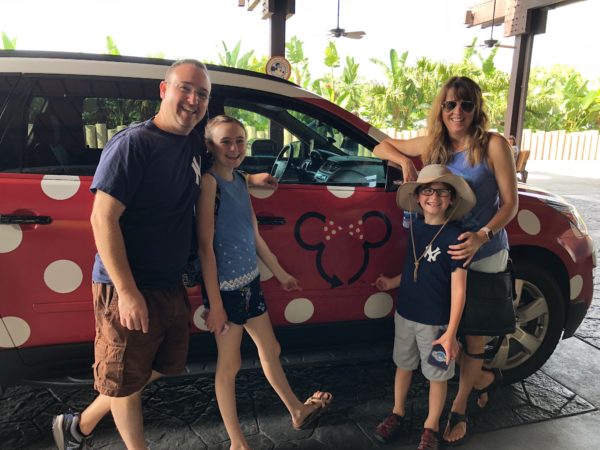 a family posing for a picture next to a red car