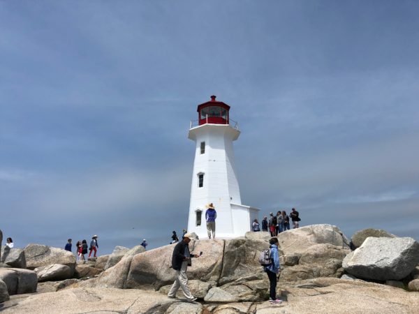 a group of people standing on rocks near a lighthouse