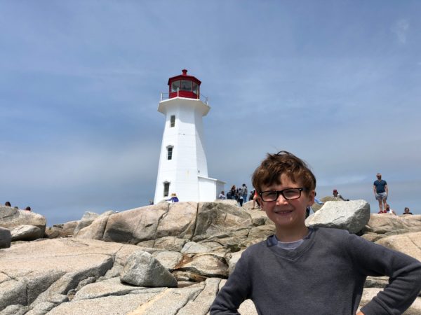 a boy standing on rocks with a lighthouse in the background