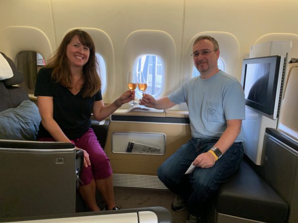 a man and woman sitting on an airplane with glasses of wine